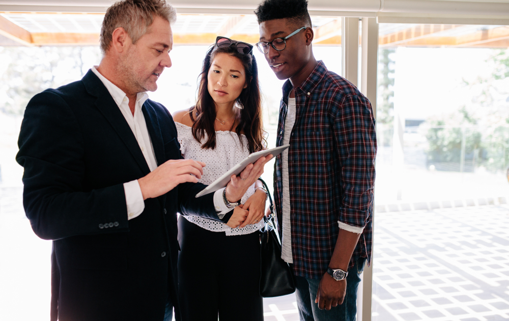 Realtor showing a young couple a house on a tablet.