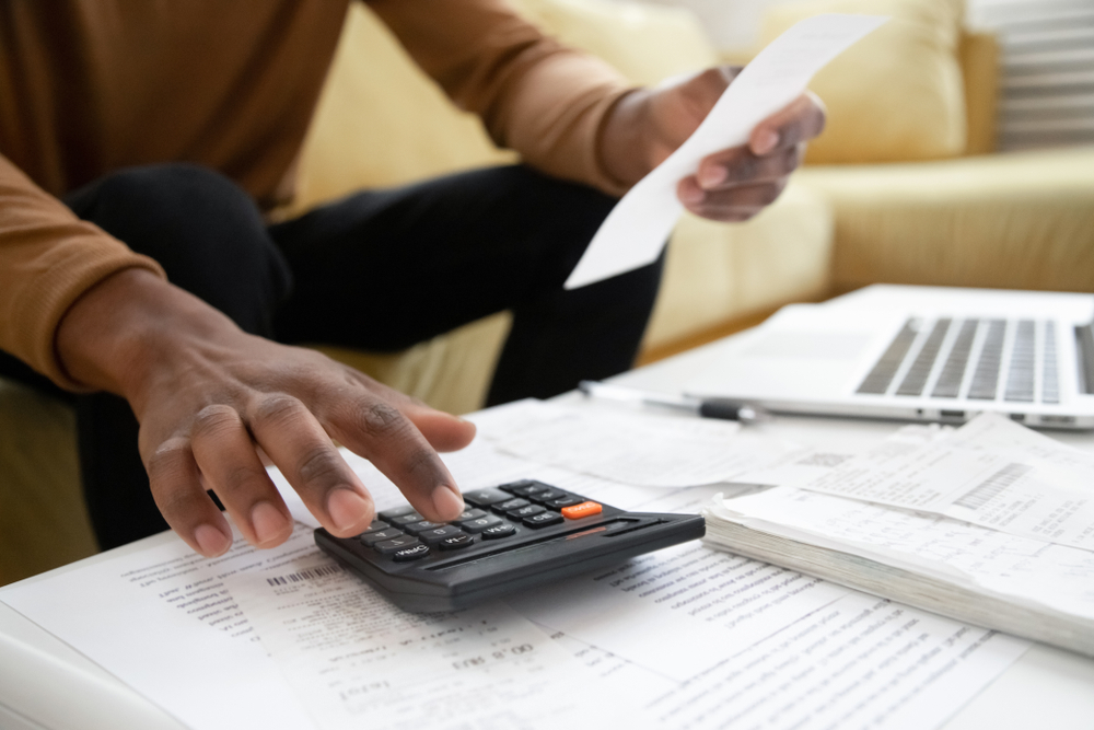Close up of hand typing on calculator that sits atop a table full of bills