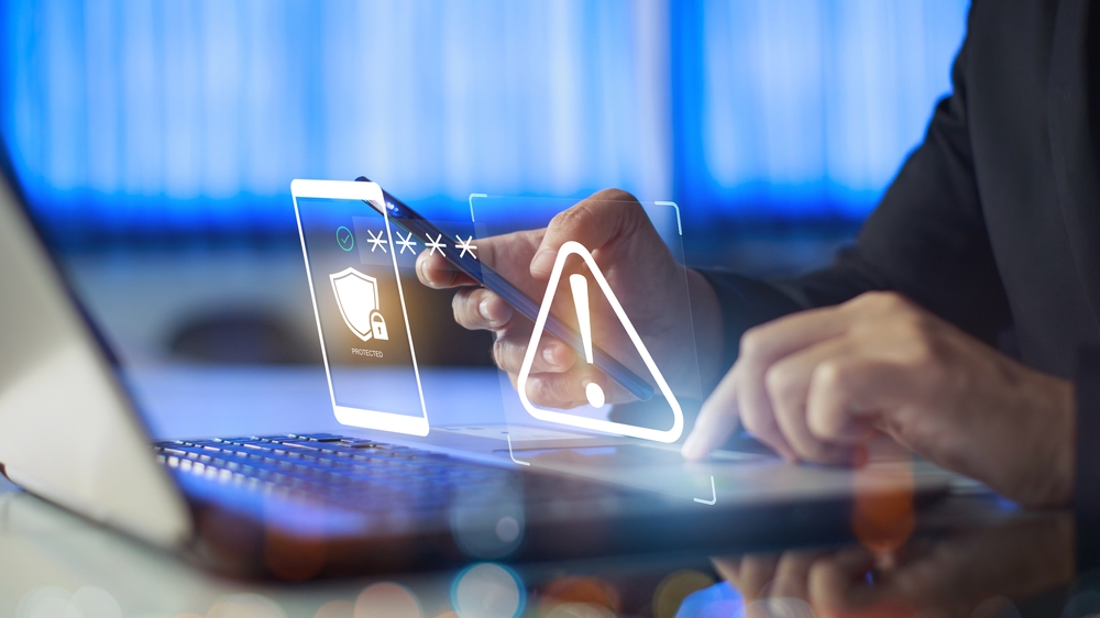 Close-up of hands holding a phone and typing on a computer with security imagery graphics on top